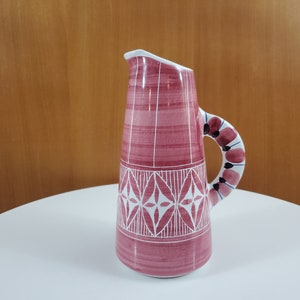May include: A pink ceramic jug with a white geometric design and a floral patterned handle.