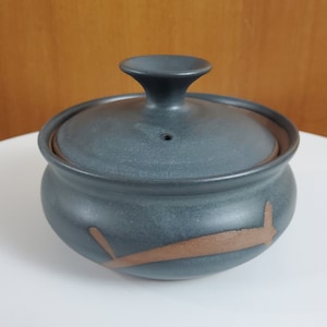 Peut inclure: Un plat de service en céramique gris foncé avec un couvercle et un motif brun. Le plat a une forme ronde et un petit bouton sur le couvercle.