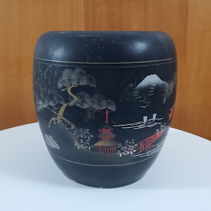 May include: Black ceramic vase with a Japanese-inspired design featuring a mountain, trees, and a red bridge. The vase has a glossy finish and is decorated with gold and white accents.