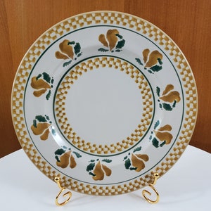 May include: A white ceramic plate with a gold and green checkered border and a repeating pattern of stylised green and gold leaves. The plate is on a gold metal stand.