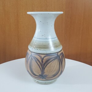 May include: A white ceramic vase with a brown and black abstract design. The vase has a wide mouth and a narrow neck.