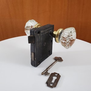 May include: Vintage door hardware set with a black metal mortise lock, clear glass doorknobs, and brass fittings. Includes a skeleton key and keyhole cover. The doorknobs have a faceted design.