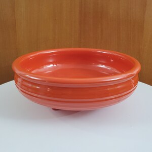 May include: A bright orange ceramic bowl with a rounded bottom and three small feet. The bowl has a smooth, glossy finish.