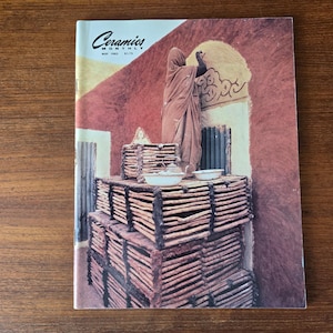 May include: A vintage copy of "Ceramics Monthly" magazine from May 1985. The cover features a person in a brown robe, with stacked wooden structures and ceramic pieces. The background is a warm, reddish-brown.