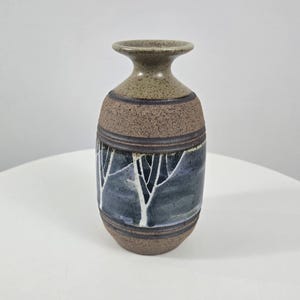 May include: A ceramic vase with a textured brown and green finish. The vase features a dark blue and white tree design around the middle. The vase is a decorative item.