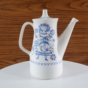 May include: White ceramic coffee pot with a blue and green floral design featuring a woman in a dress. The design includes flowers, leaves, and geometric patterns.