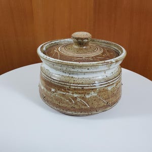 May include: A brown and white ceramic casserole dish with a lid. The dish has a speckled glaze and a simple design.