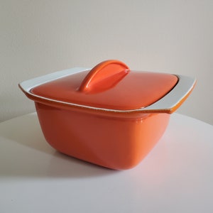 May include: Orange ceramic casserole dish with a white rim and a white handle. The dish has a lid.