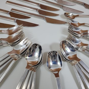 May include: A set of silver cutlery, including forks, spoons, and knives, arranged in a circular pattern on a white surface.