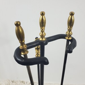 May include: A black metal fireplace tool set with three brass-tipped tools. The tools are attached to a black metal stand.
