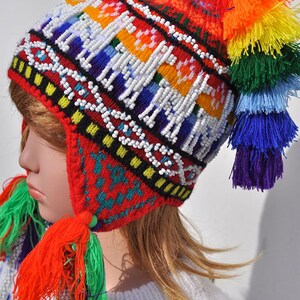 May include: A red knitted hat with colorful tassels and white beads. The hat has a geometric pattern and is decorated with a rainbow of colors.