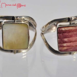 Puede incluir: Dos anillos de plata con incrustaciones de forma cuadrada. El anillo de la izquierda tiene una incrustación de nácar blanco. El anillo de la derecha tiene una incrustación de madera rosa y blanca.