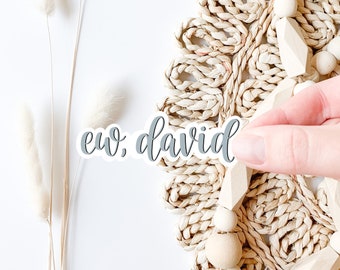 May include: A gray vinyl sticker with the text "ew, david" in a cursive font. The sticker is placed on a woven straw mat with wooden beads.