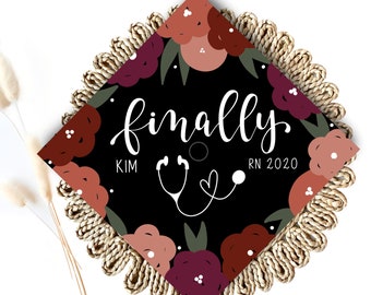May include: Black graduation cap with a floral design in shades of red, pink, and brown. The text "finally" is written in white cursive script with a stethoscope and heart graphic. The text "KIM RN 2020" is also written in white.