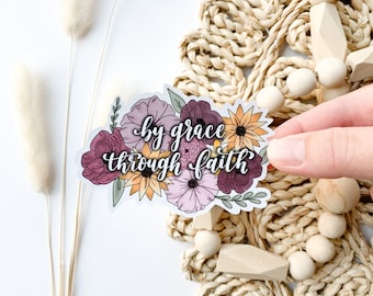 May include: A white sticker with a floral design and the text "by grace through faith" in black calligraphy.