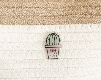 May include: A green cactus in a pink pot with the text "FREE HUGS" on a white and beige woven background.