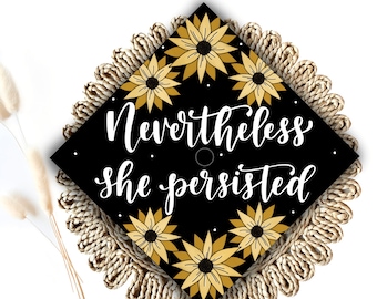 May include: Black graduation cap with a gold floral design and the text "Nevertheless she persisted".