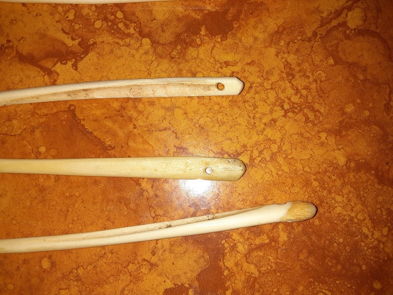 May include: Three wooden knitting needles with a hole at the end of each needle. The needles are on a brown surface.