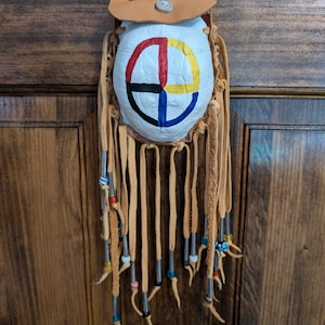 May include: A small, white leather pouch with a painted symbol and fringe. The pouch is hanging from a brown leather strap.