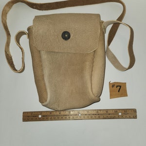 Puede incluir: Un bolso de cuero marrón claro de bandolera con cierre de solapa y un solo botón. El bolso tiene una correa larga y está etiquetado con el número "7".