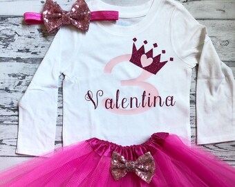 Può includere: Un tutù di tulle rosa con un fiocco di glitter rosa e oro. Una maglietta bianca a maniche lunghe con un numero 3 rosa, una corona rosa con un cuore e il nome "Valentina" in glitter rosa. Un cerchietto rosa con un fiocco di glitter rosa e oro.