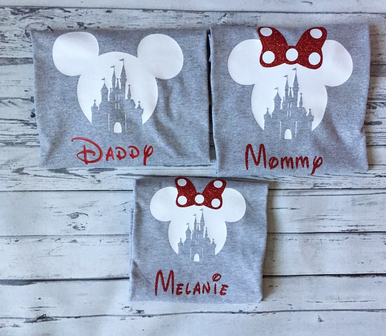 May include: Three grey t-shirts with a white silhouette of Mickey Mouse ears and Cinderella's castle. The shirts have red glitter text that says "Daddy", "Mommy", and "Melanie".