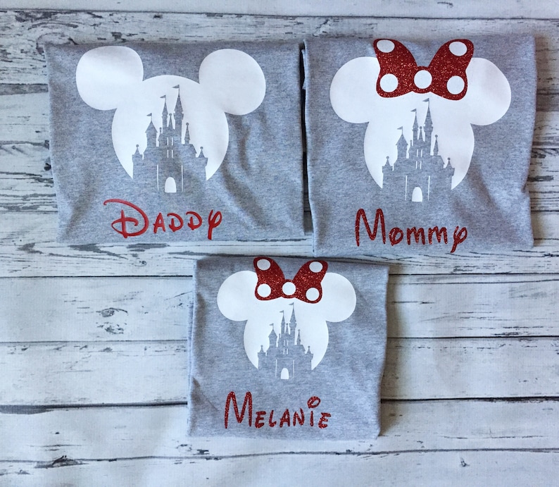 May include: Three grey t-shirts with a white silhouette of Mickey Mouse ears and Cinderella's castle. The shirts have red glitter text that says "Daddy", "Mommy", and "Melanie".