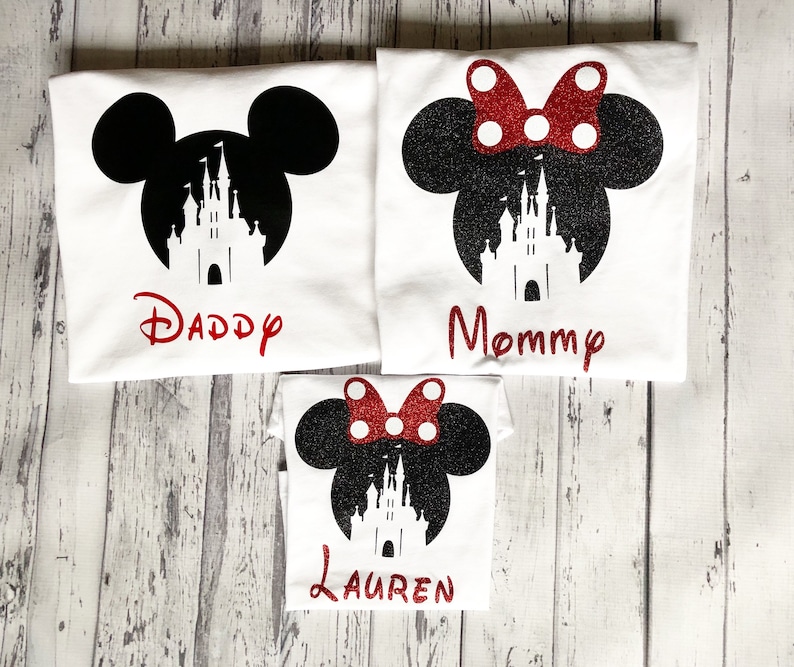 May include: Three white t-shirts with black Mickey Mouse ears and a silhouette of Cinderella's castle. The shirts have the words "Daddy", "Mommy", and "Lauren" printed on them.