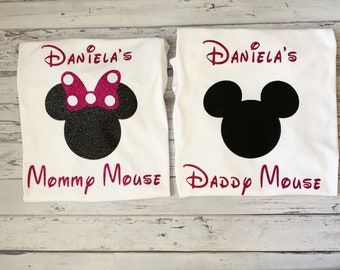 May include: Two white t-shirts with a pink glitter design. One shirt says "Daniela's Mommy Mouse" with a black and white glitter Minnie Mouse head. The other shirt says "Daniela's Daddy Mouse" with a black glitter Mickey Mouse head.