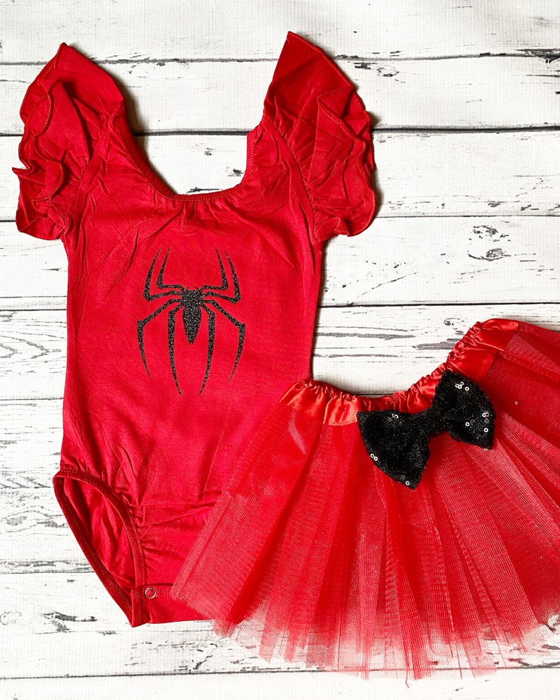 May include: Red and black spider-themed baby outfit with a red leotard with a black spider graphic and a red tulle skirt with a black sequin bow.