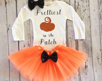 May include: Orange tulle tutu skirt with a black bow and a white long-sleeved onesie with the text "Prettiest in the Patch" and a glitter pumpkin graphic.