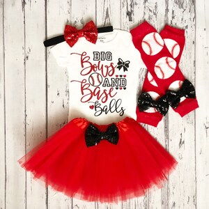 Puede incluir: Un conjunto de bebé niña de temática de béisbol en rojo y blanco. El conjunto incluye un body blanco con el texto "Big Bows and Base Balls" en purpurina negra y roja, una falda de tul roja con un lazo de lentejuelas negras, una diadema roja con un lazo de lentejuelas rojas y polainas rojas y blancas con pelotas de béisbol impresas.