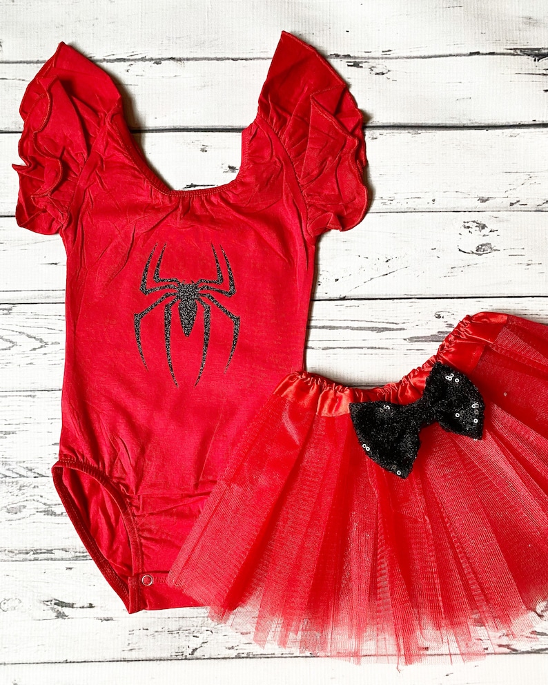 May include: Red and black spider-themed baby outfit with a red leotard with a black spider graphic and a red tulle skirt with a black sequin bow.