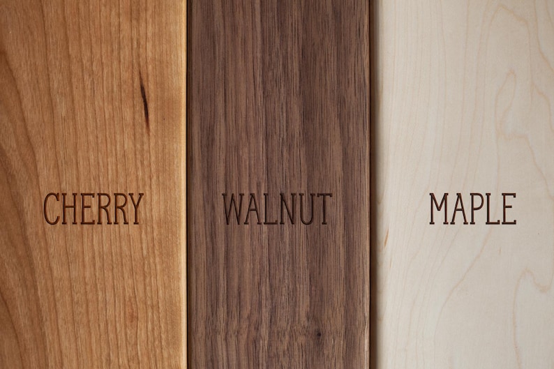 K&ouml;nnte beinhalten: Nahaufnahme von drei Holzbrettern: Kirsche, Walnuss und Ahorn. Das Kirschbrett ist hellbraun, das Walnussbrett dunkelbraun und das Ahornbrett hellbeige. Jedes Brett hat die Holzart in Gro&szlig;buchstaben eingraviert.