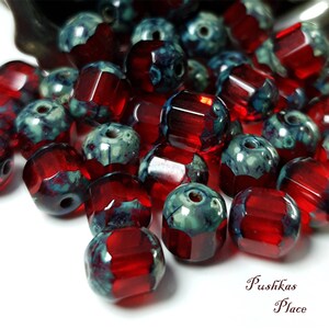 May include: A collection of red and blue glass beads with a faceted design. The beads have a mottled, marbled effect.