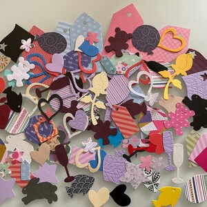 May include: A large collection of assorted paper die-cut shapes in various colours and patterns. The assortment includes hearts, stars, flowers, rabbits, fish, teddy bears, wine glasses, and rectangular tags, featuring textures and prints.