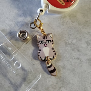 May include: A gold retractable badge holder with a red and white circular charm that says "platelet party!" and a grey and black cat charm with a gold chain.
