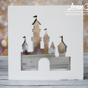 Könnte beinhalten: Weißer Holzausschnitt eines Schlosses mit dekorativem Design. Das Schloss ist aus dem Holz ausgeschnitten, wodurch ein Schatteneffekt entsteht. Das Holz ist weiß lackiert und das Schloss befindet sich in der Mitte des Bildes.