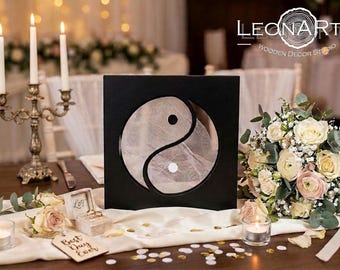 Może przedstawiać: Kwadratowa czarna drewniana ramka z okrągłym wycięciem i symbolem yin-yang. Środek zawiera półprzezroczysty, teksturowany materiał z małą czarną kropką i małą białą kropką. Widoczne jest logo LEONARTS WOODEN DECOR STUDIO.