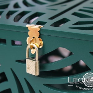 May include: A dark green wooden box featuring intricate laser-cut patterns, a gold-coloured metal latch, and a small brass padlock. The bottom right corner displays the white text LEONARTS WOODEN DECOR STUDIO with a circular tree ring graphic.