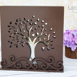 Könnte beinhalten: Eine braune Holzkiste mit einem ausgeschnittenen Design eines Baumes mit Blättern. Die Kiste hat unten ein dekoratives Schriftrollen-Design. Die Kiste steht auf einer weißen Oberfläche. Der Text "LEONARTS WOODEN DECOR STUDIO" ist in der oberen rechten Ecke des Bildes sichtbar.