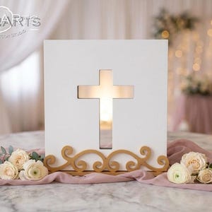 May include: A square white wooden plaque featuring a central cutout in the shape of a cross. The plaque is supported by a decorative gold-colored base with swirling scrollwork patterns. The text LEONARTS WOODEN DESIGN STUDIO is visible.