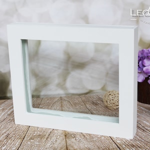 May include: White picture frame with a clear glass insert. The frame is sitting on a wooden surface.