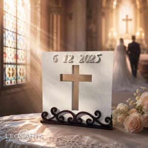 May include: A white square plaque featuring a cutout cross in the center and the raised numbers 6 12 2025 at the top. The plaque is supported by a dark brown wooden base with decorative scrollwork along the bottom edge.