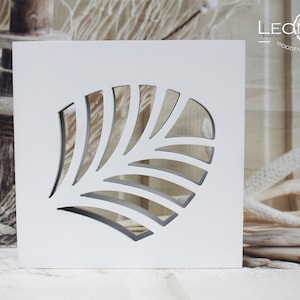 May include: White wooden wall decor with a cutout design of a stylised leaf. The design is reminiscent of a seashell. The text "LEONARTS WOODEN DECOR STUDIO" is printed at the top of the decor.
