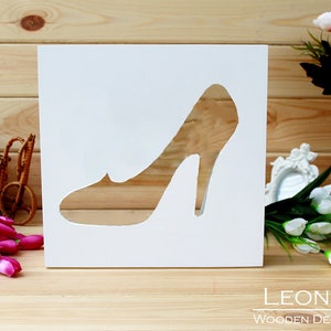 Könnte beinhalten: Weiße Holz-Wanddekoration mit einem Ausschnitt einer hochhackigen Schuhs. Die Dekoration befindet sich auf einer Holzoberfläche mit rosa und weißen Blumen.