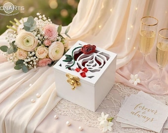 May include: A square white wooden box with a gold-coloured metal latch. The lid features a cutout rose design with a red rose and green leaves. The box is positioned near a bouquet of pink and white flowers, two champagne flutes, and cards with the text forever & always.