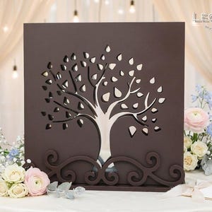 Peut inclure: Un panneau carré en bois brun foncé présentant un motif d'arbre découpé au laser avec des formes de feuilles ouvertes. La base du panneau possède une bordure décorative à volutes. Le logo LEONARTS WOODEN DESIGN STUDIO est imprimé en haut à droite.