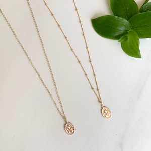 May include: Two gold necklaces with oval pendants. The pendants feature a religious image. The necklaces are on a white background.