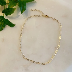 May include: A gold chain necklace with a delicate, oval-shaped link design. The necklace has an adjustable clasp.